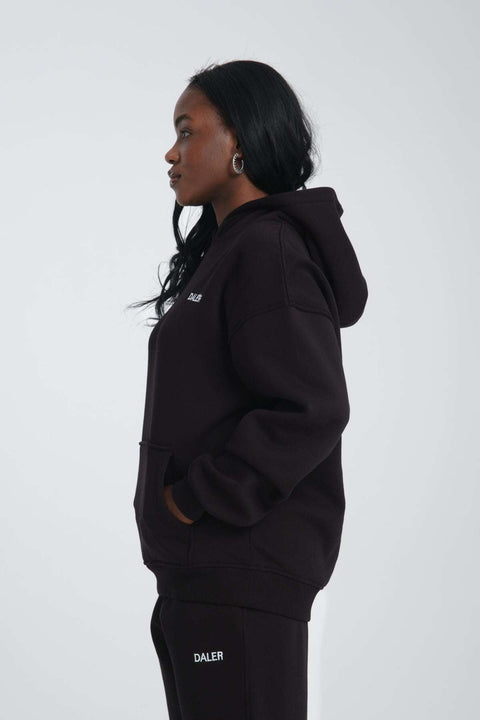 2. Side view of woman in black oversized hoodie with DALER logo, hands in pockets, studio background