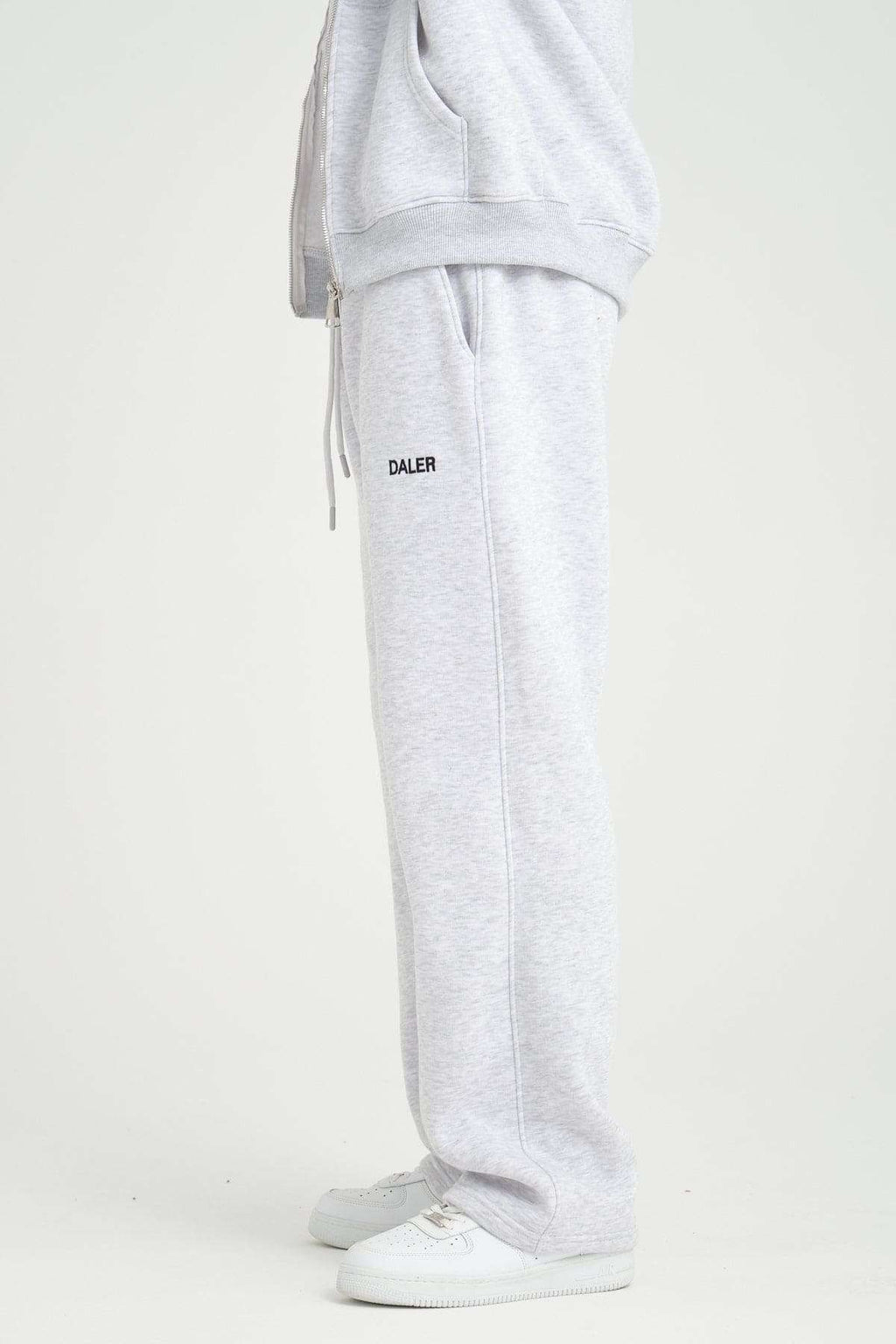 2. Side view of grey melange jogger pants with DALER logo, paired with white sneakers