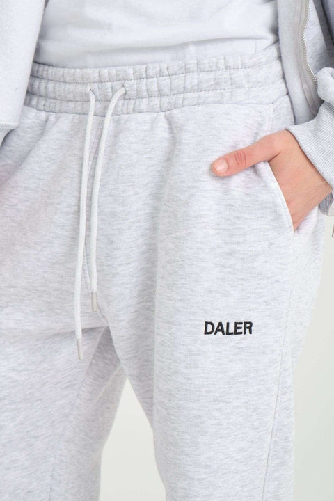 3. Close-up of grey melange jogger pants with DALER embroidery and drawstring waist, hand in pocket