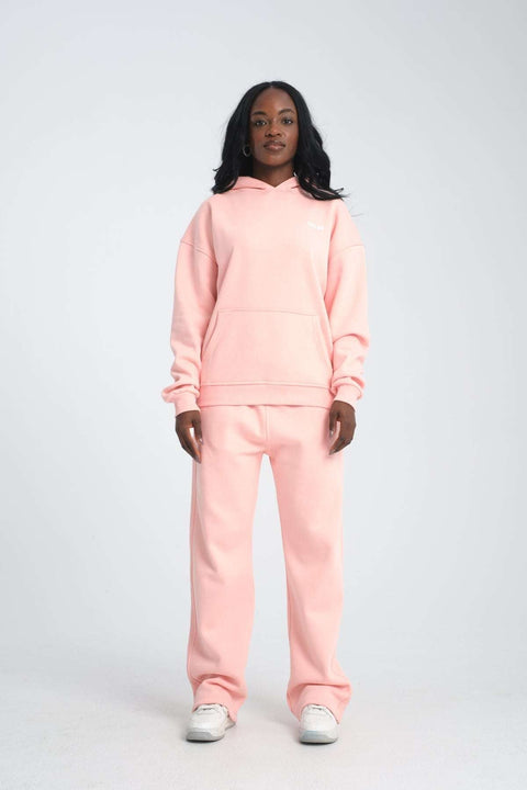 2. Woman in pink oversized hoodie and matching pants, standing with arms relaxed, against a plain background