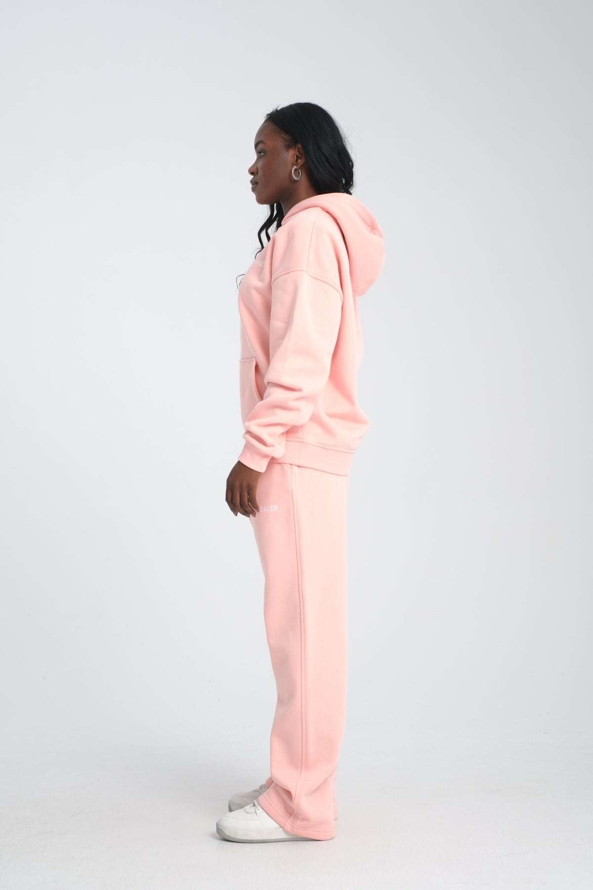 2. Side view of woman in pink oversized hoodie and matching pants, standing against a plain background