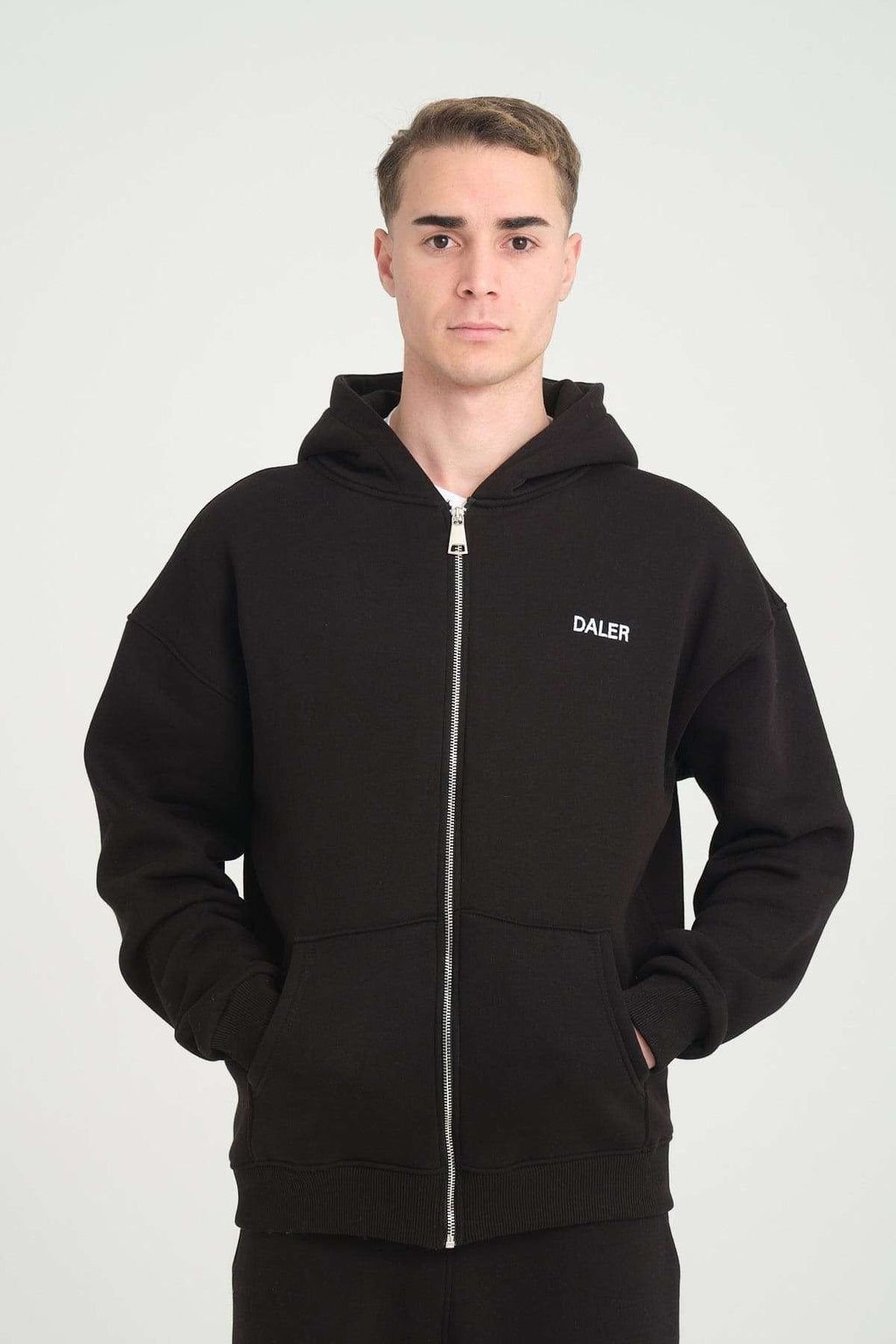 1. Man wearing black DalerClo heavyweight zipper hoodie with DALER embroidery, hands in pockets, studio setting