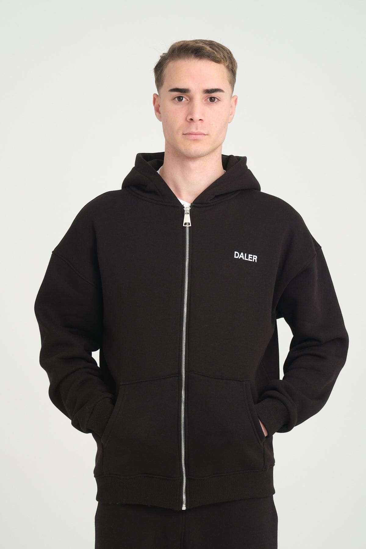 1. Man wearing black DalerClo heavyweight zipper hoodie with DALER embroidery, hands in pockets, studio setting