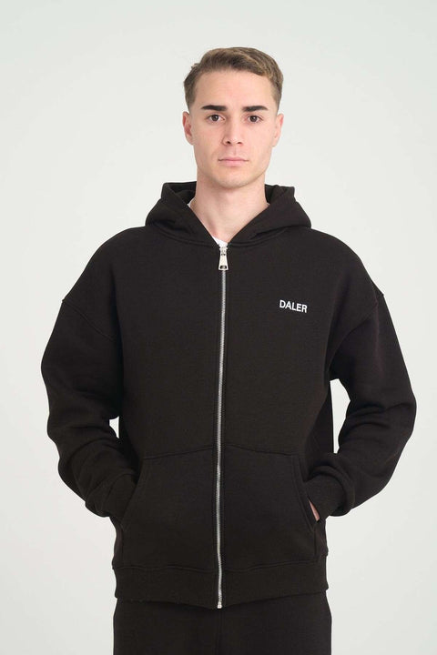 1. Man wearing black DalerClo heavyweight zipper hoodie with DALER embroidery, hands in pockets, studio setting