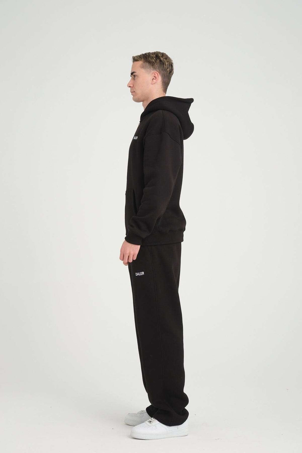 2. Side profile of man wearing black DalerClo heavyweight zipper hoodie and pants, studio setting