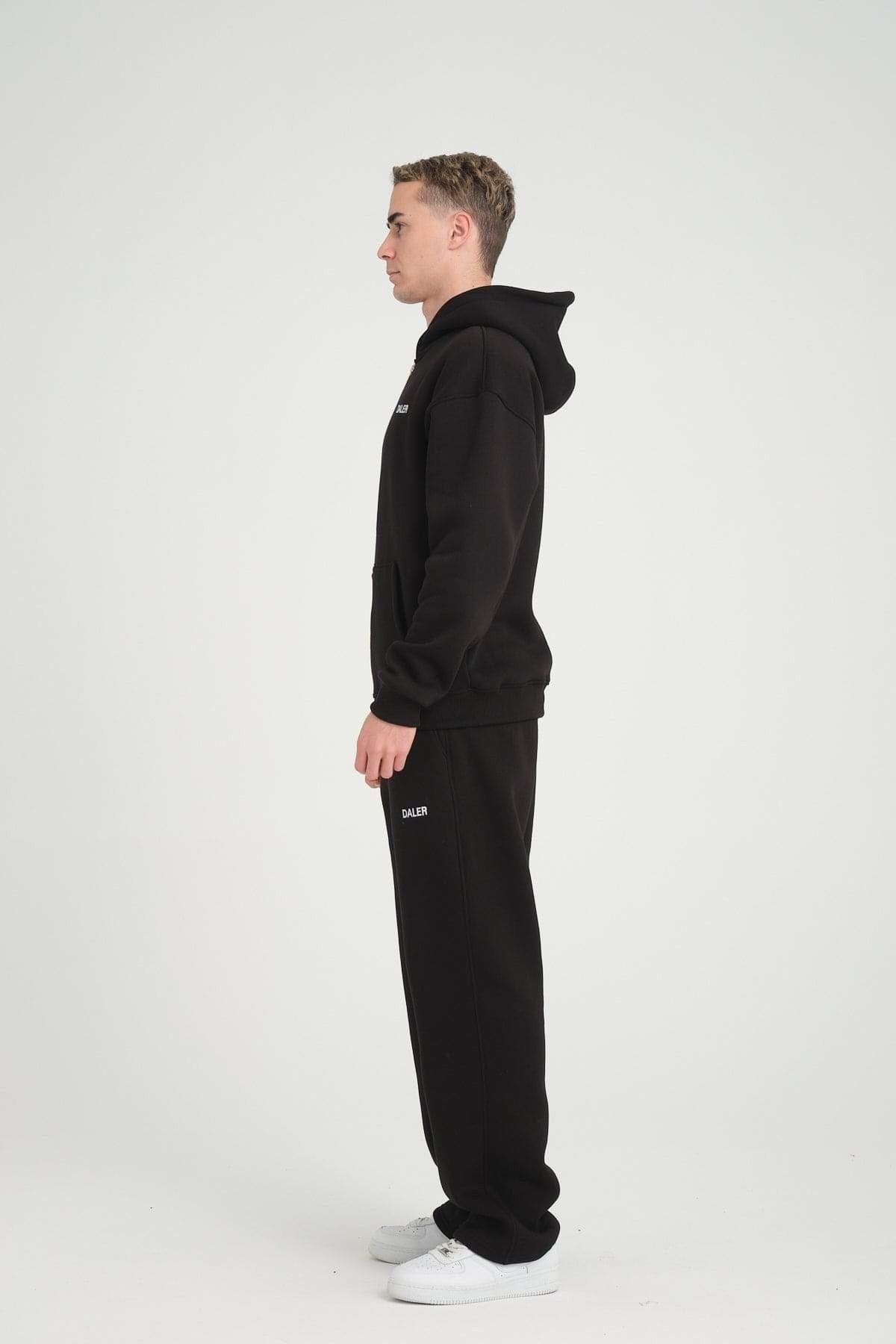 2. Side profile of man wearing black DalerClo heavyweight zipper hoodie and pants, studio setting