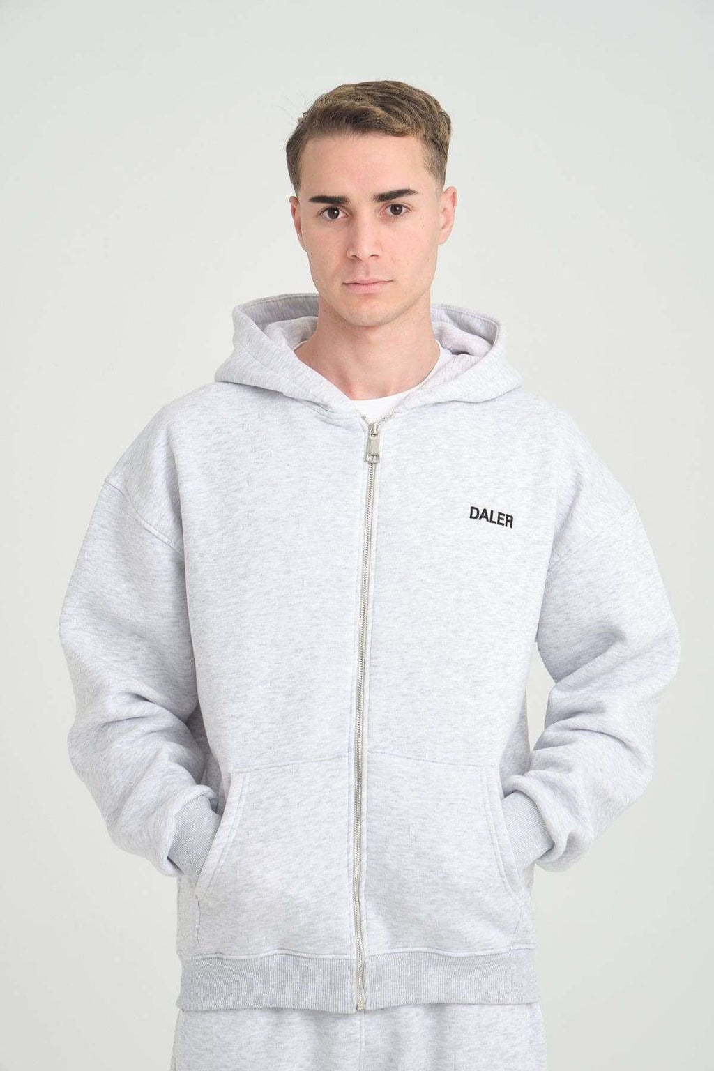 1. Man wearing grey melange DalerClo hoodie with DALER embroidery, hands in pockets, studio setting