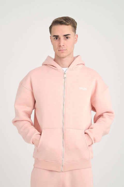 1. Man wearing pink oversized zipper hoodie with DALER embroidery on chest, hands in pockets, studio background