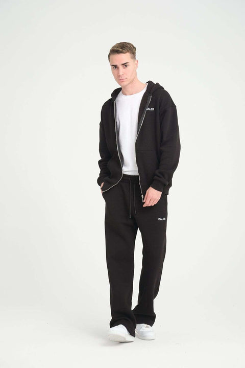 2. Man wearing black jogger pants and matching hoodie with DALER logo, standing in studio