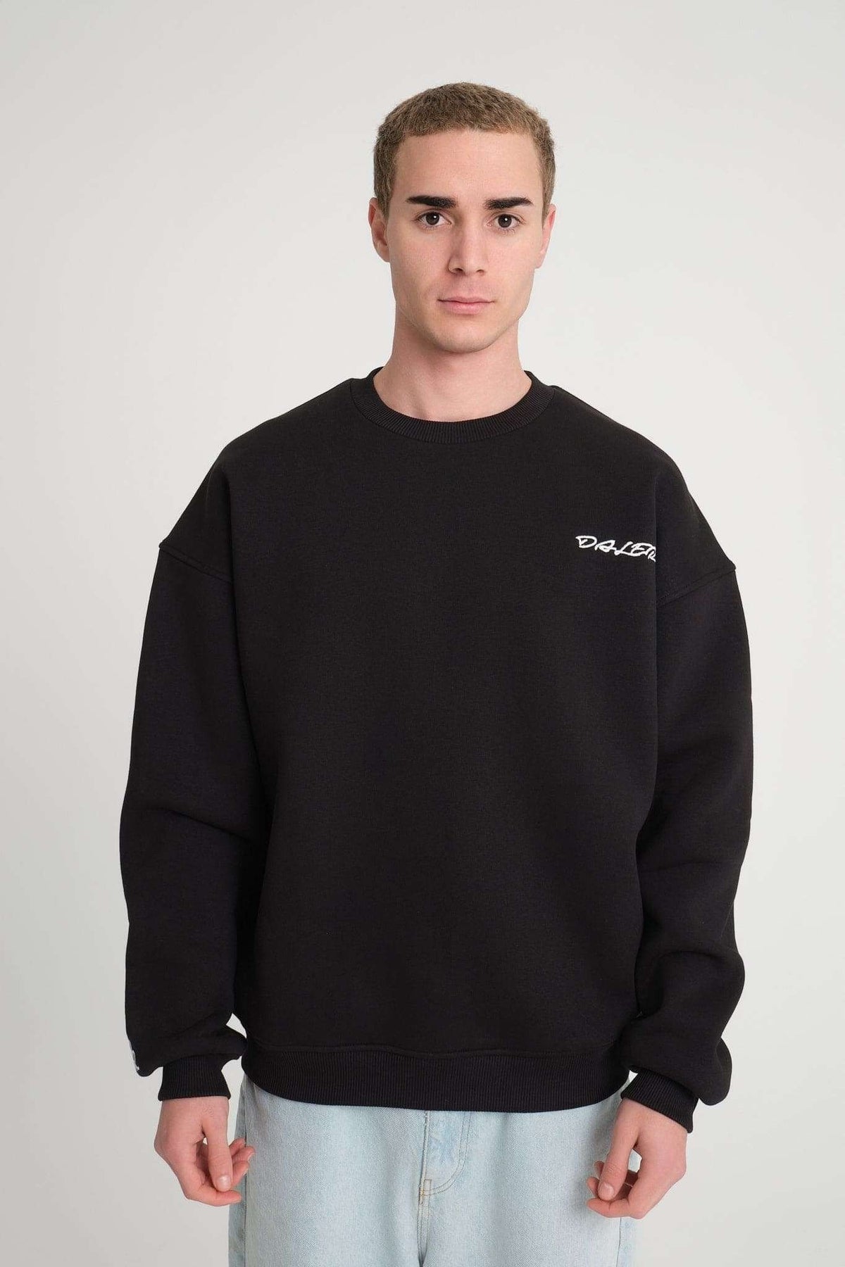 1. Man wearing black oversized DalerClo sweatshirt with chest embroidery, standing against a plain background