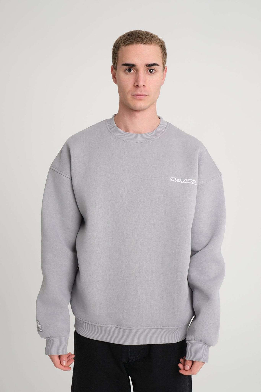 1. Man wearing grey oversized DalerClo sweatshirt with white embroidery on chest, standing in studio setting