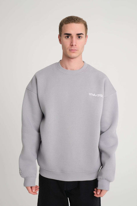 1. Man wearing grey oversized DalerClo sweatshirt with white embroidery on chest, standing in studio setting
