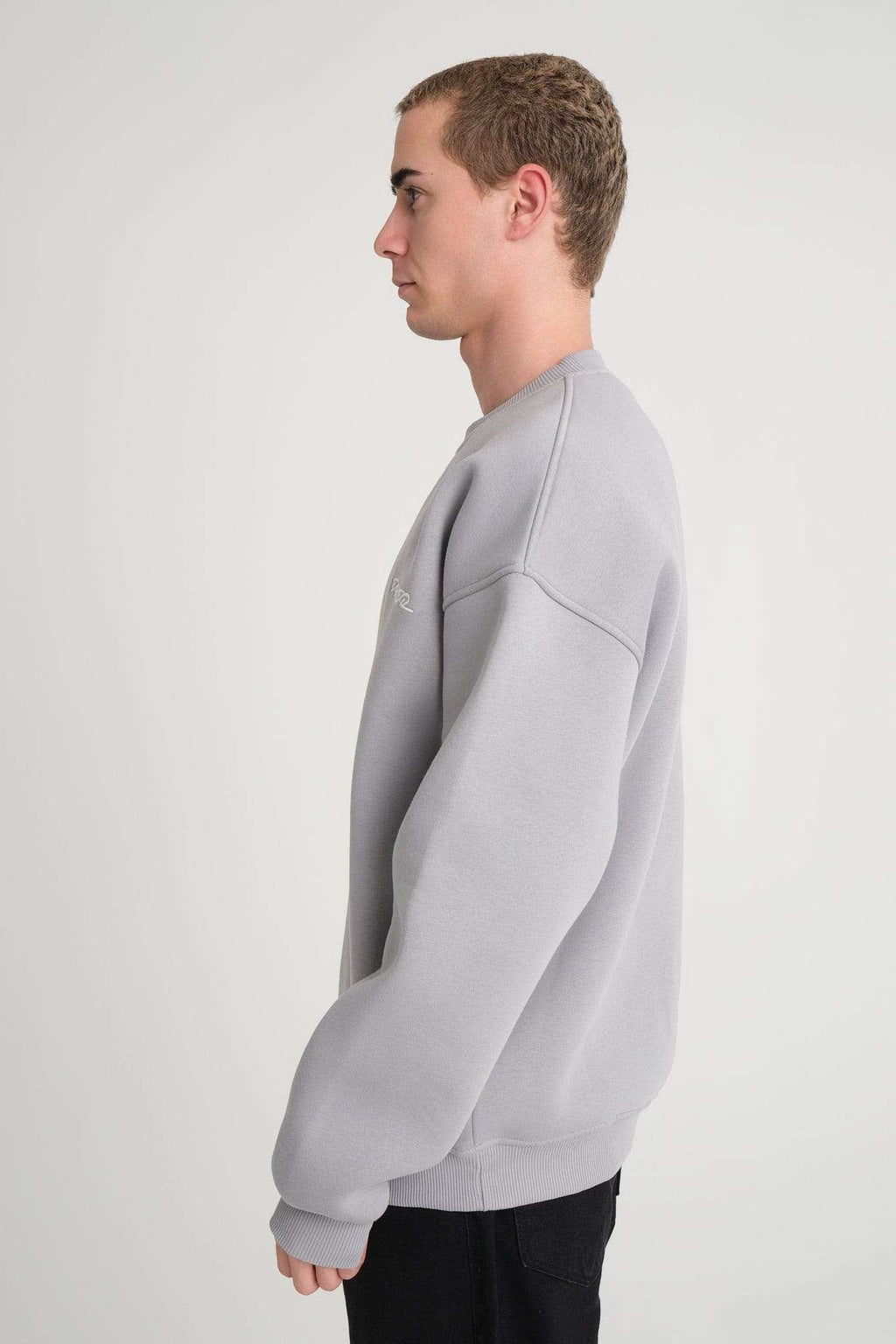 2. Side view of man wearing grey oversized DalerClo sweatshirt in studio setting