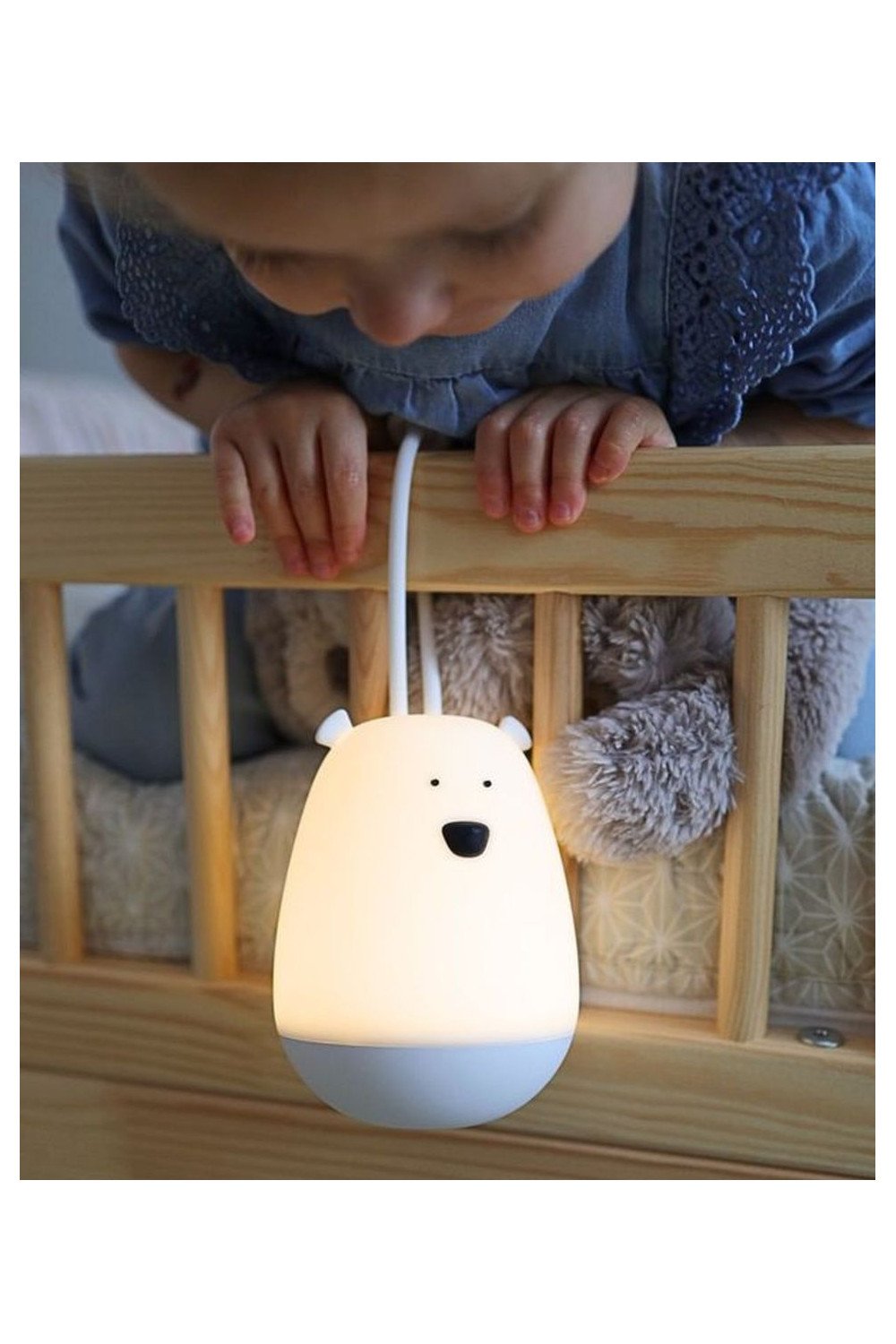 6. Child leaning over a crib with a glowing white bear-shaped night light hanging on the rail