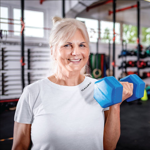 1. Woman wearing Beebila embroidered collar organic cotton t-shirt in white, holding a blue dumbbell in a gym setting
