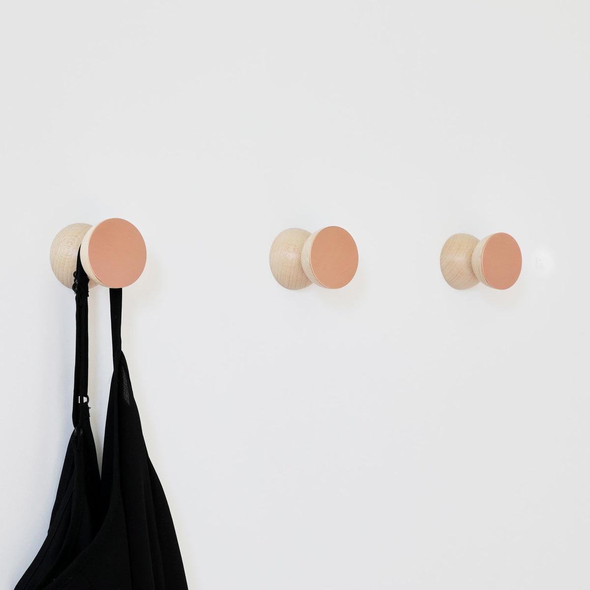 2. Beech Wood & Copper Wall Hooks by 5mm Paper, mounted on wall holding a black garment