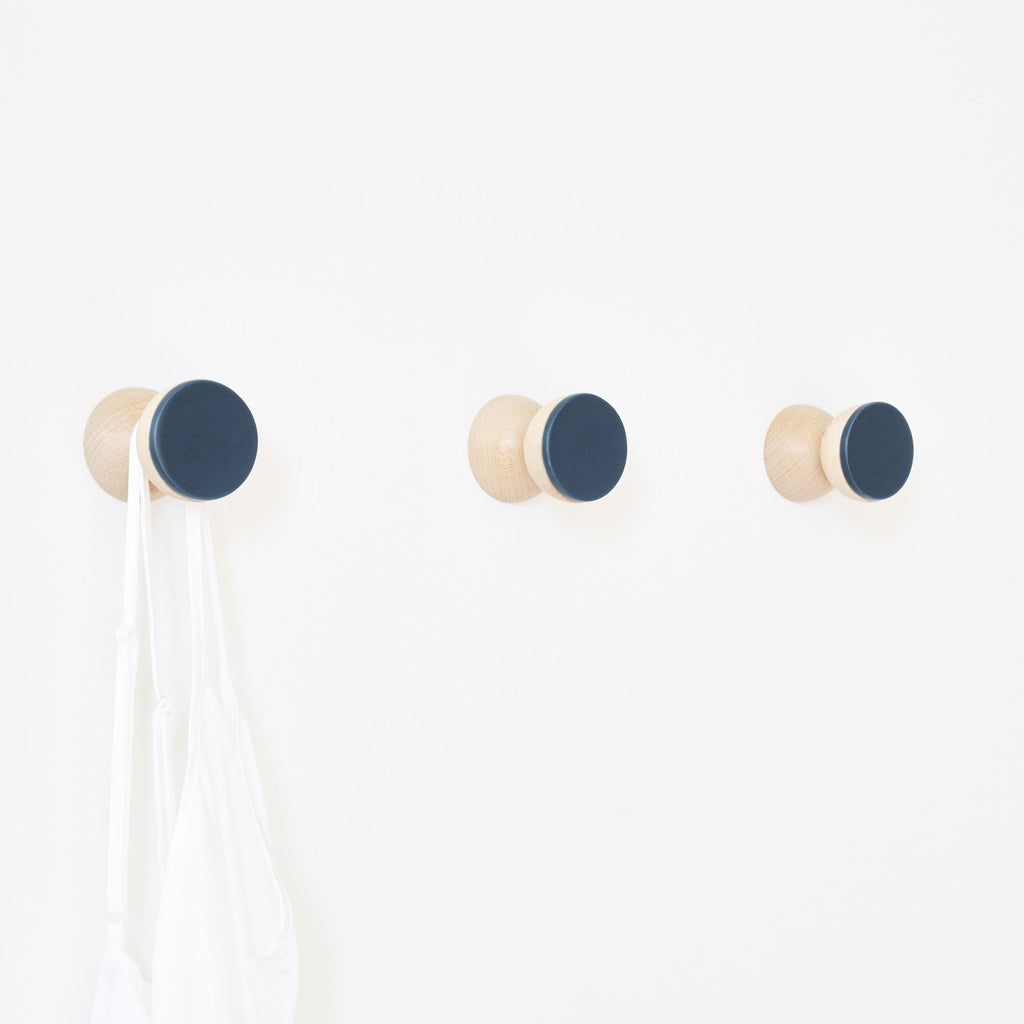 1. Trio of 5mm Paper beech wood and dark blue ceramic wall hooks holding a white bag, showcasing minimalist design on a white wall
