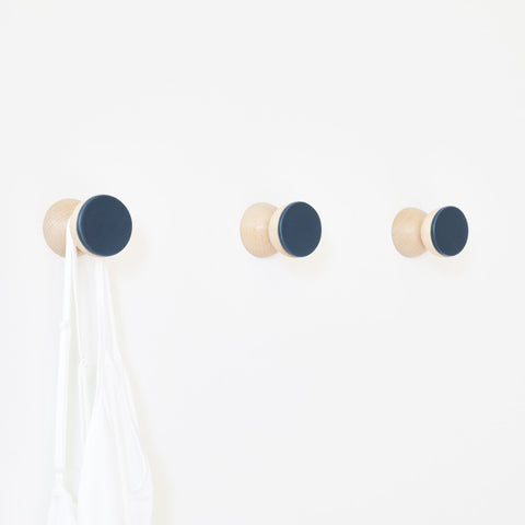 1. Trio of 5mm Paper beech wood and dark blue ceramic wall hooks holding a white bag, showcasing minimalist design on a white wall