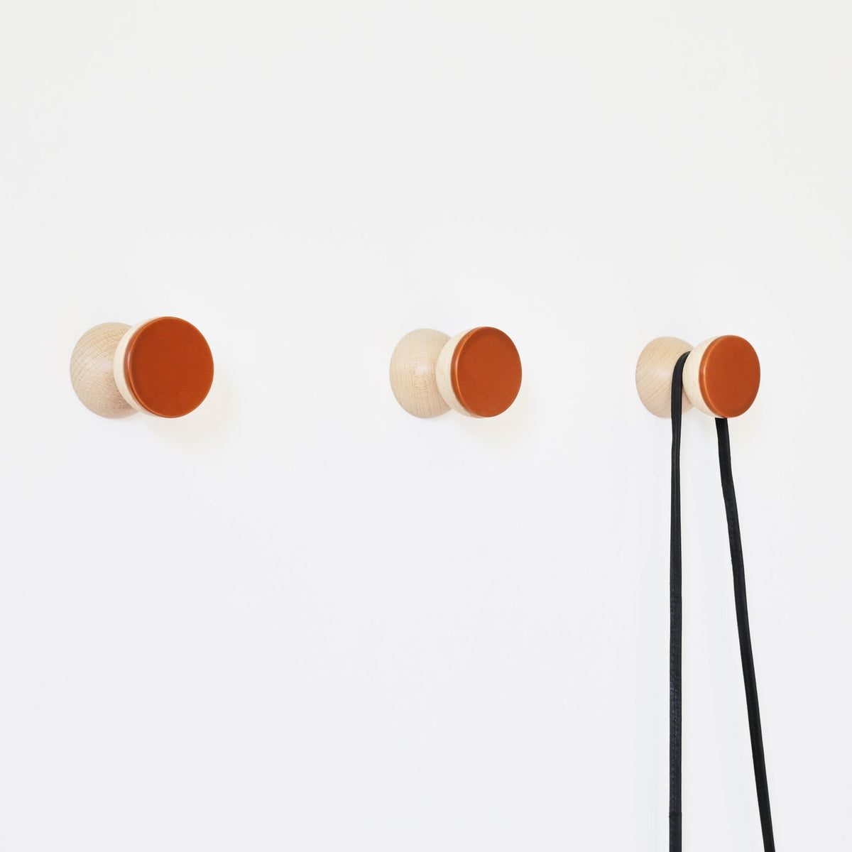 3. Studio image of Beech Wood & Ceramic Wall Hooks by 5mm Paper in dark terracotta orange, shown with a black cable hanging
