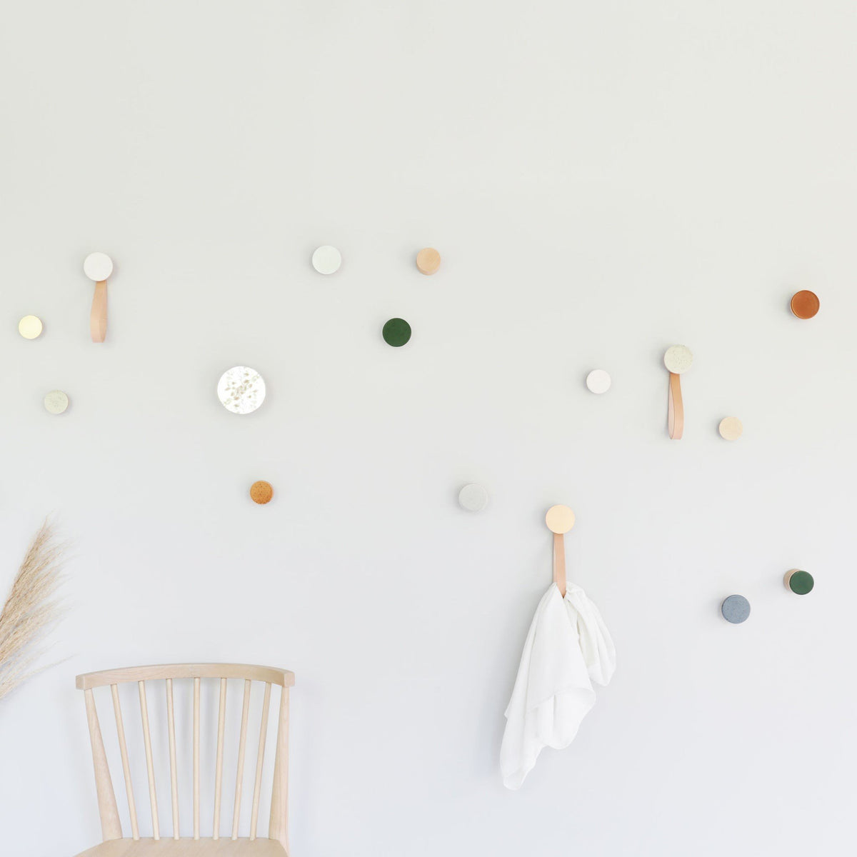 2. Lifestyle image of Beech Wood & Ceramic Wall Hooks by 5mm Paper in a creative space, featuring various colors including dark terracotta orange, used for hanging items