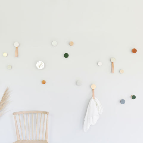 2. Lifestyle image of Beech Wood & Ceramic Wall Hooks by 5mm Paper in a creative space, featuring various colors including dark terracotta orange, used for hanging items