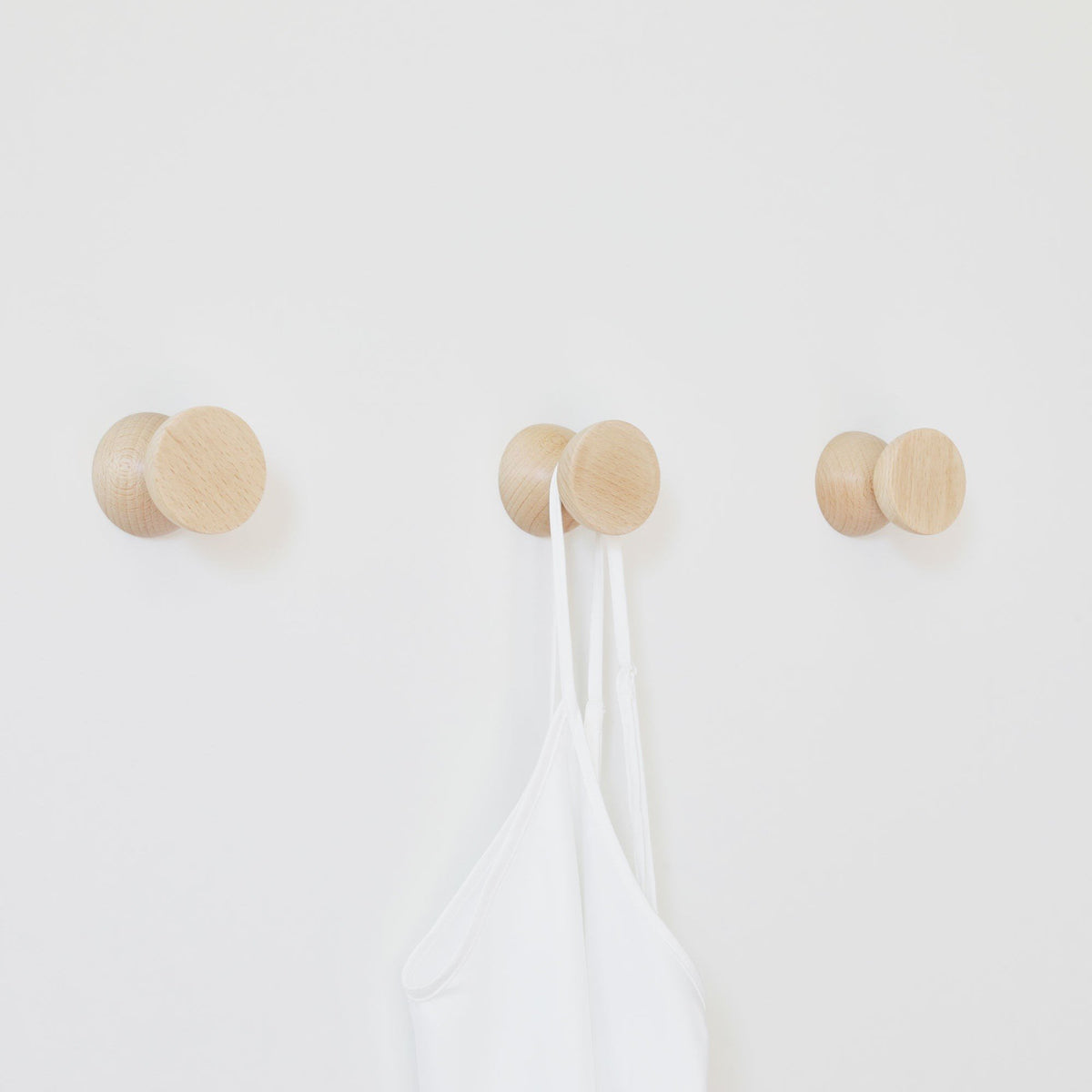 4. Studio image of three beech wood wall hooks by 5mm Paper holding a white garment