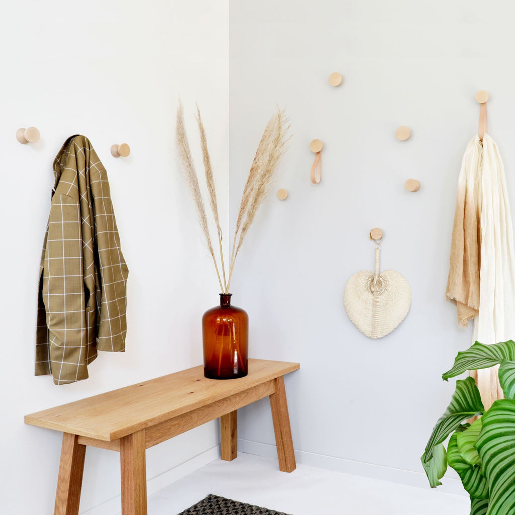 2. Lifestyle image of beech wood wall hooks by 5mm Paper in a cozy entryway with hooks holding a coat and decor