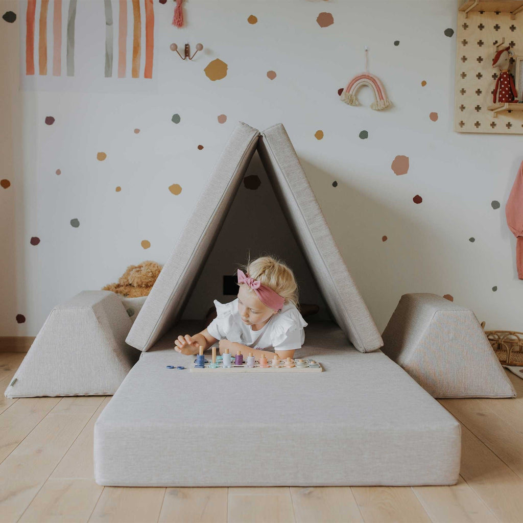 2. Child playing inside a tent made from beige Monboxy play mattress set in a decorated room