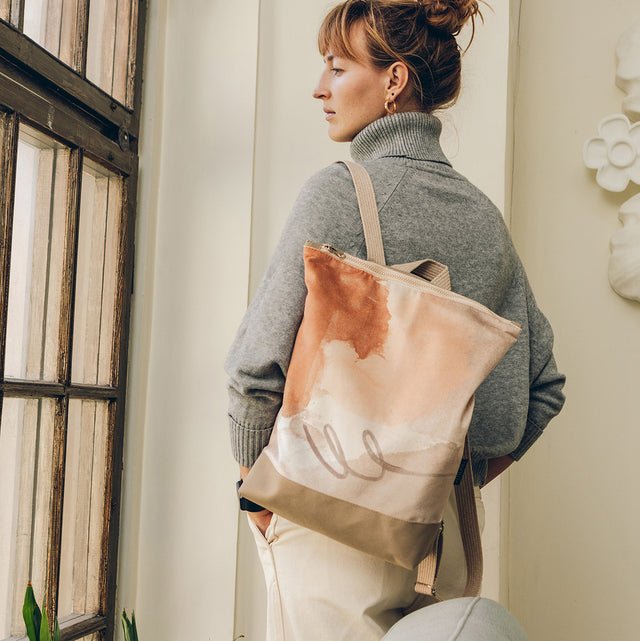 2. Woman wearing Muni Abstract Beige backpack with velvet and polyester design, standing indoors
