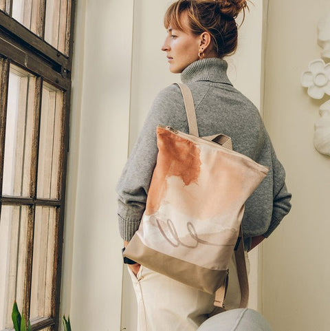 2. Woman wearing Muni Abstract Beige backpack with velvet and polyester design, standing indoors