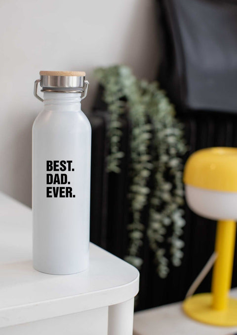2. White matte stainless steel thermos bottle with 'BEST. DAD. EVER.' text on table, featuring metal handle and bamboo lid, next to yellow lamp and plant.