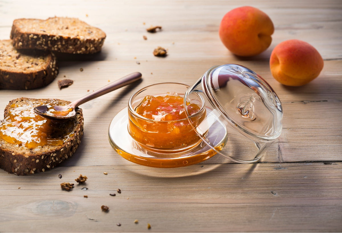 1. Transparent glass butter dish with bee design on wooden table with apricots and bread
