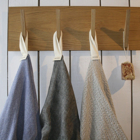 4. Three linen towels in different colors hanging on wooden hooks with KOOSdisain labels