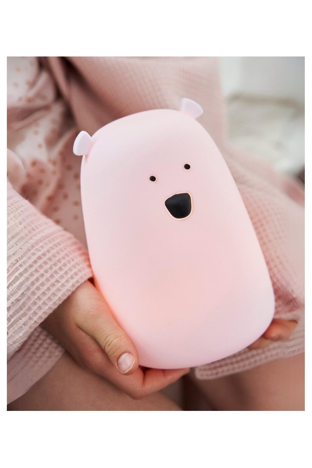 1. Child holding pink teddy bear-shaped silicone lamp with black eyes and nose, wearing a pink robe