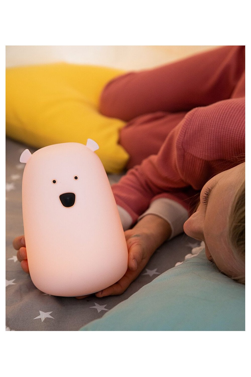1. Child lying in bed with glowing pink bear lamp, surrounded by colorful pillows
