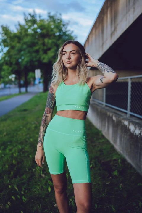 1. Woman wearing Peachlabel green biker shorts and matching top, standing outdoors