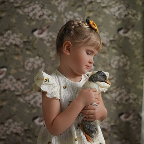 1. Young girl holding a toy duck in front of Dekornik's green spring wallpaper with birds and blossoms