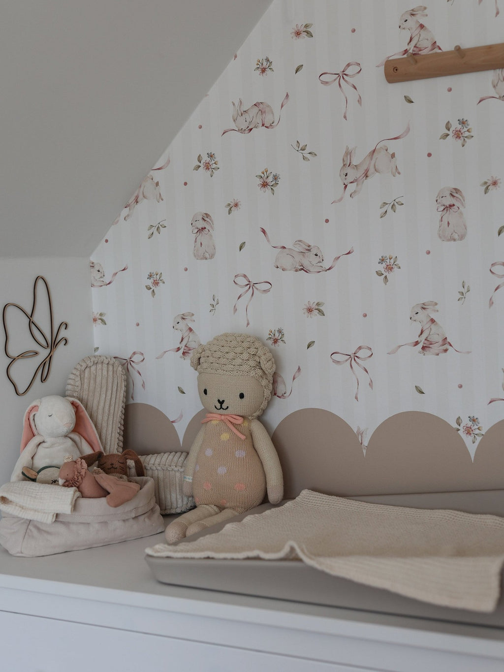 1. Nursery with pink rabbits on stripes wallpaper, plush toys, and changing table