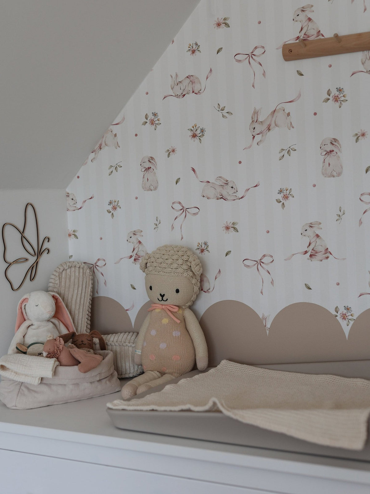 1. Nursery with pink rabbits on stripes wallpaper, plush toys, and changing table