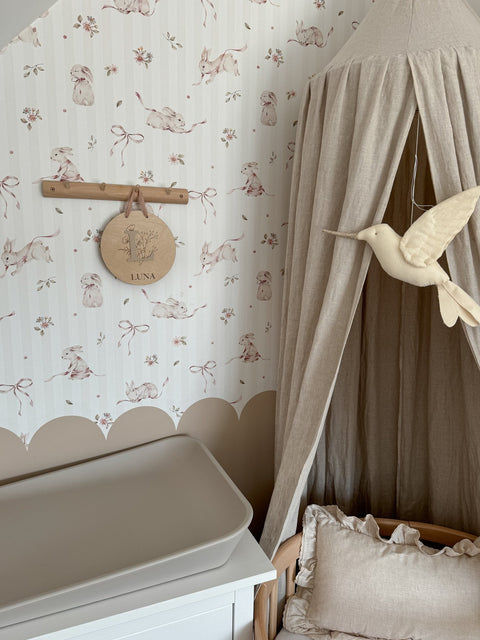 1. Nursery corner with pink rabbits on stripes wallpaper, beige canopy, and bird decor