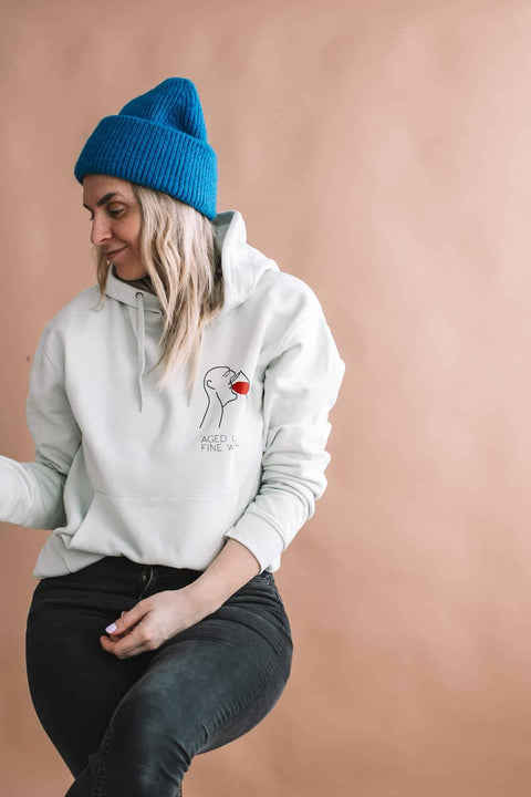 2. Woman in Black Giraffe Brand 'Aged Like Fine Wine' hoodie, light green, with blue beanie, studio setting