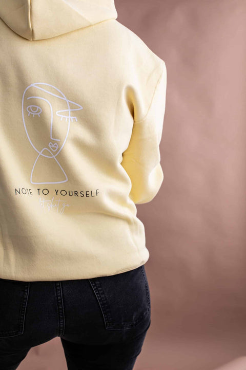 2. Back view of Black Giraffe Brand Note to Self Hoodie in light yellow, featuring line art and 'Note to Yourself' text