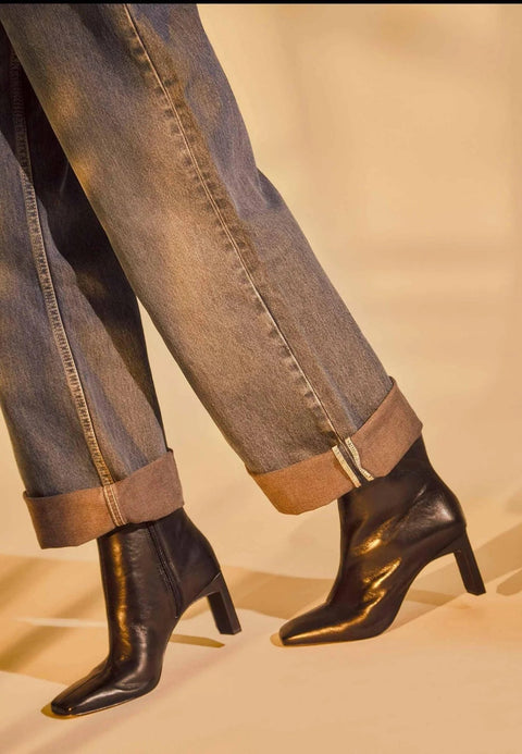 1. Person wearing black goat leather Senna boots with 7.6 cm block heel and rolled-up jeans in warm lighting