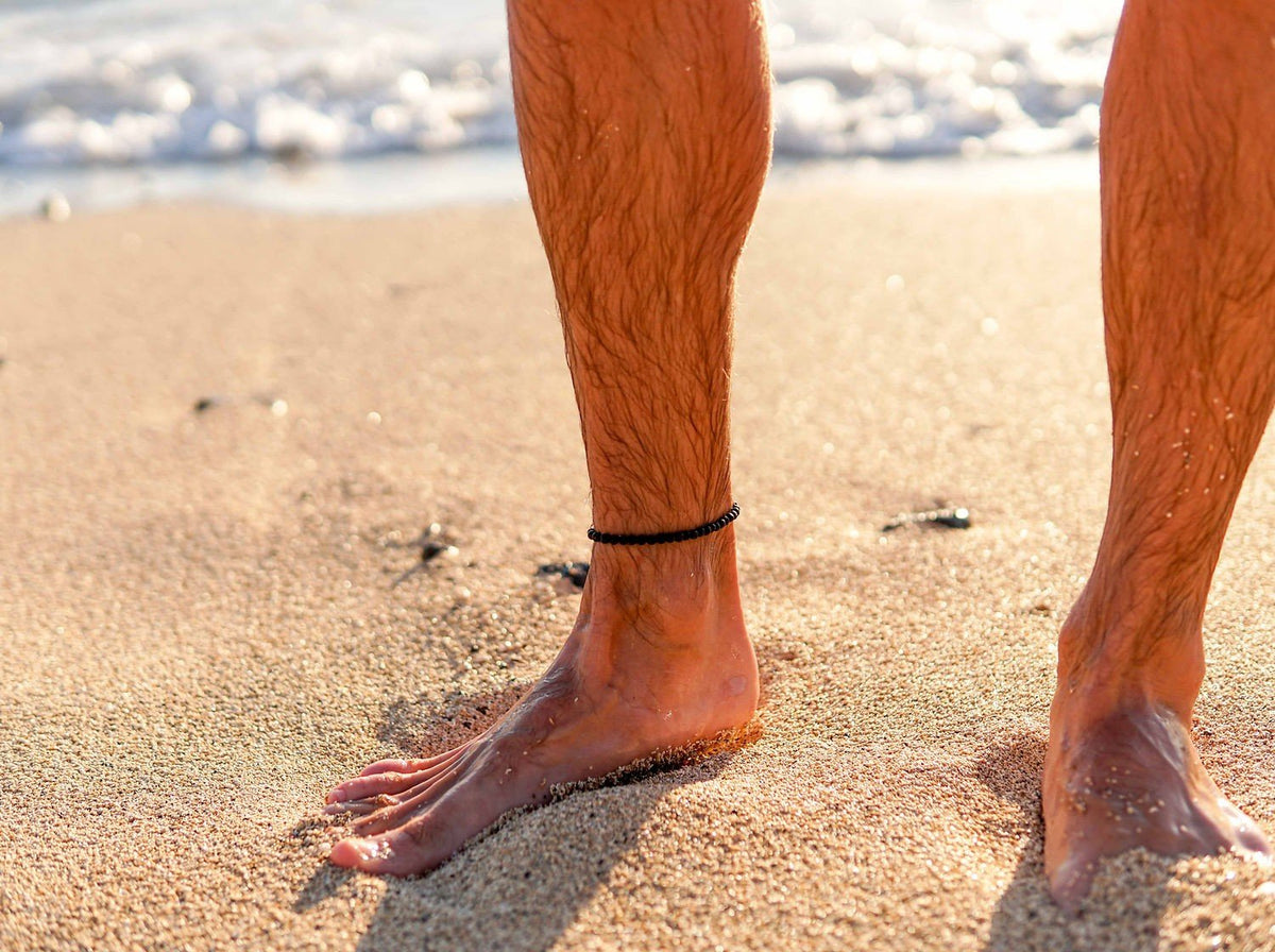 1. Men's Black Lava Anklet by Canary Lava worn on beach, showcasing rugged elegance and natural sophistication