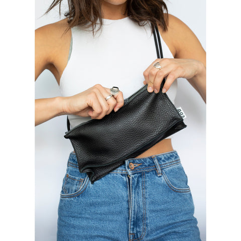 1. Woman holding Daz Studio handmade black leather bum bag with adjustable strap, styled with white top and denim jeans