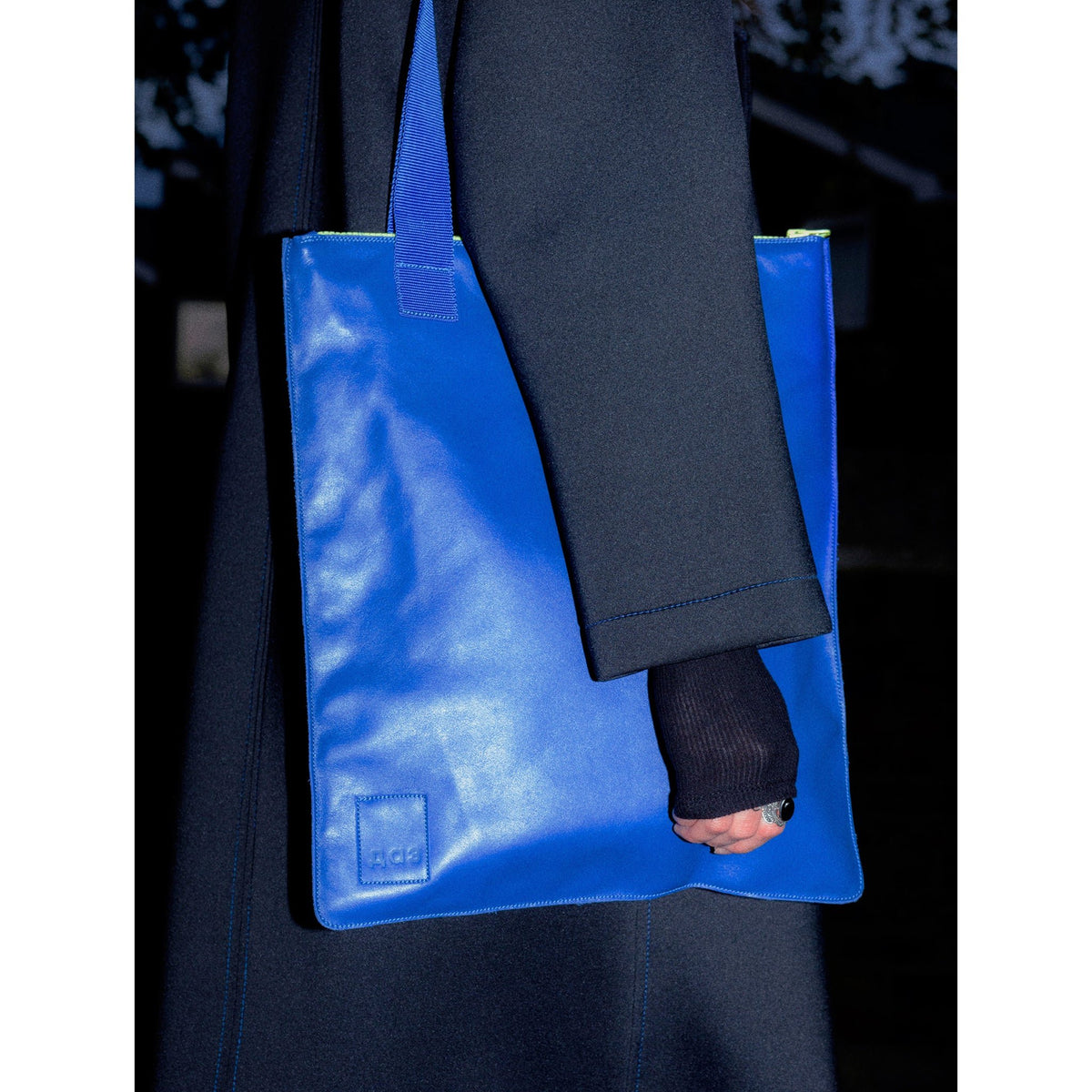 3. Daz Studio royal blue leather tote worn by woman in dark coat, highlighting neon green zipper