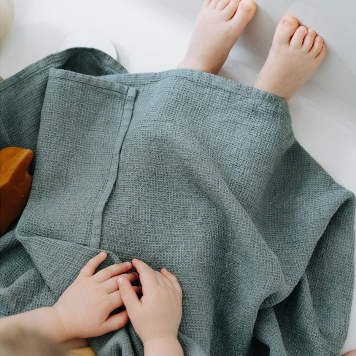 2. Close-up of child's feet and hands under a blue waffle linen towel