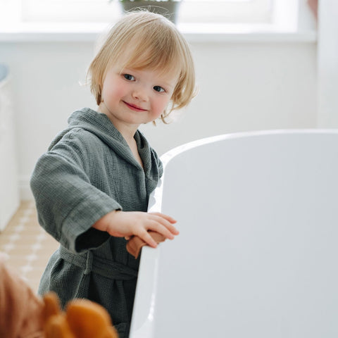 4. Smiling child in blue fog linen bathrobe with hood by bathtub