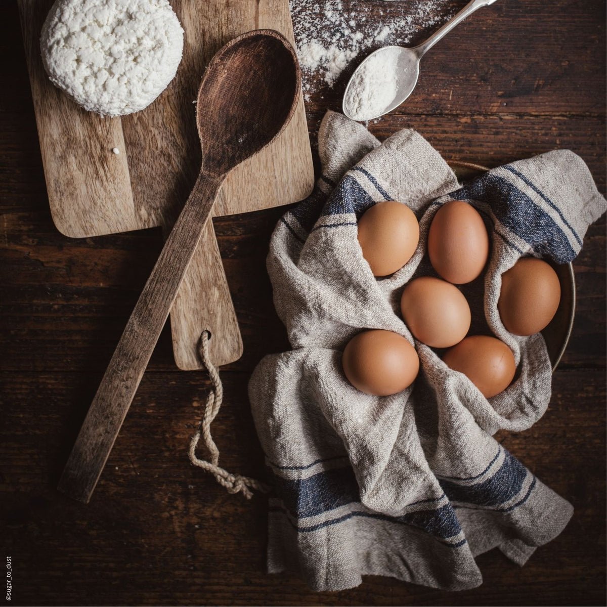 2. Rustic kitchen scene with beige linen towel with blue stripes holding eggs on wooden table