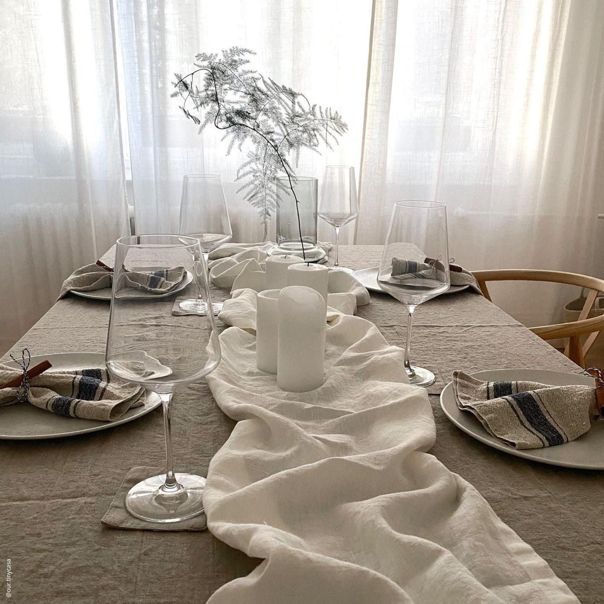 7. Minimalist table setting with blue striped linen napkins, wine glasses, and white candles on linen tablecloth